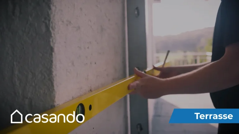 Eine Person hält eine gelbe Wasserwaage gegen eine weiße Wand, während sie WPC-Terrassendielen verlegt.
