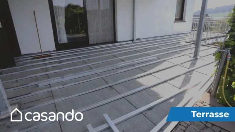 Grau-braune WPC-Terrassendielen werden parallel auf Metallrahmen neben einem Haus verlegt.