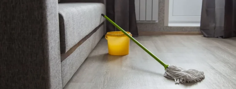 Ein gelber Eimer und ein Mopp auf einem aufgeräumten Holzboden.