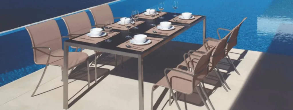 In dem Bild ist eine moderne Outdoor-Essgruppe am Poolrand zu sehen. Der Fokus liegt auf einem stilvollen Gartentisch mit schwarzer Oberfläche, um den sechs beige Stühle gruppiert sind. Auf dem Tisch sind elegante Platzdeckchen in Beige gestaltet, darauf stehen weiße Schüsseln und Teller sowie Besteck aus Edelstahl, sorgfältig arrangiert. Im Hintergrund schimmert das kräftige Blau des Pools sanft im Sonnenlicht und verleiht der Szene eine ruhige Atmosphäre. Die Kombination aus den neutralen Farben der Möbel und dem lebendigen Blau des Wassers schafft ein harmonisches Gesamtbild.