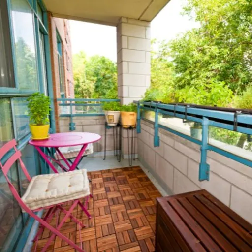 Balkon mit rosa Möbeln, Pflanzen, kleinen Bäumen und modernem Balkonboden sichtbar.