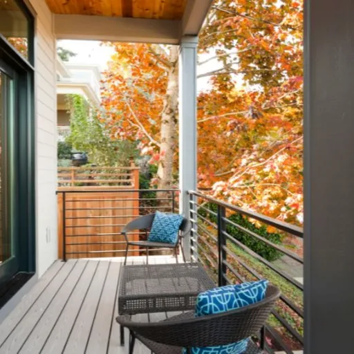 Balkon mit Stühlen, Tisch und modernem Holzboden, Herbstbäume mit orangefarbenen Blättern draußen.