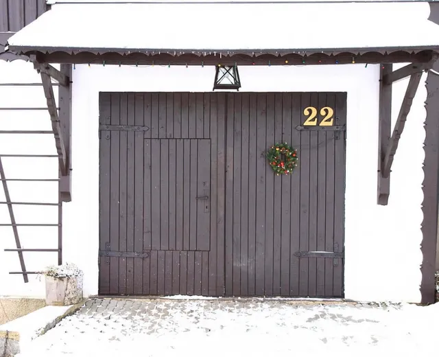 Braune hölzerne Garagentore mit einem grünen Kranz und der Nummer 22 darüber, heller Wandhintergrund.