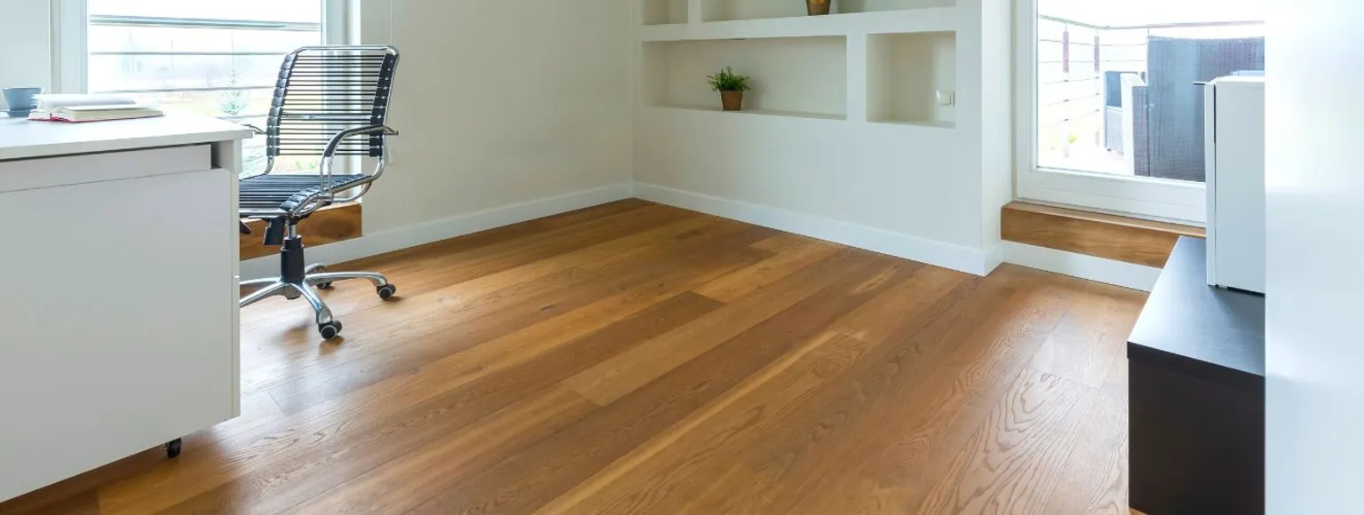 Büroeinrichtung mit Vinylboden, weißem Schreibtisch, schwarzem Stuhl, Regalen und Fensterbeleuchtung.