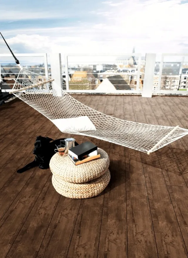 Dachterrasse mit Hängematte, geflochtenen Poufs, HPL-Tisch, Büchern, Getränken und Blick auf die Stadt.