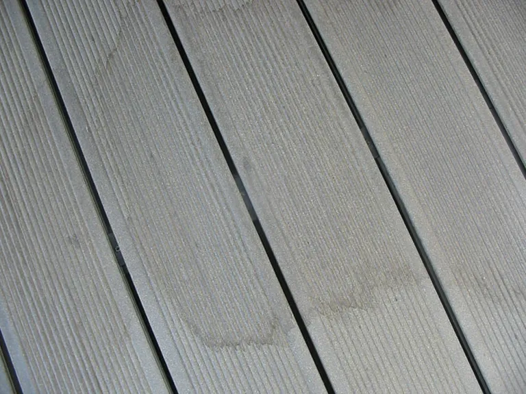 Detailaufnahme einer grauen WPC-Terrasse mit Wasserflecken und strukturierten Rillen im Außenbereich.