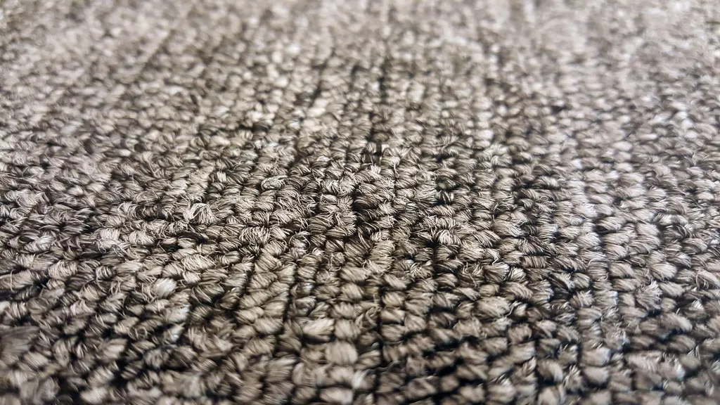 Detailaufnahme eines grauen Schlingenfaserteppichs neben einem hellen Parkettboden im Innenbereich.