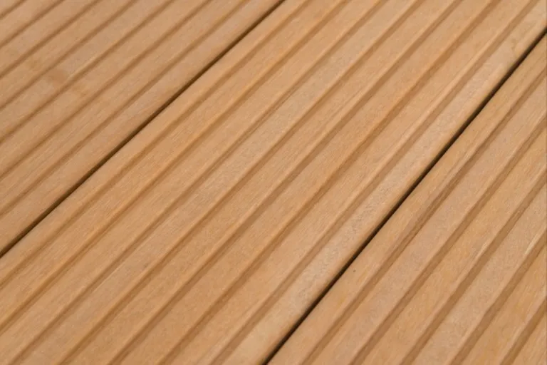 Detailaufnahme von hellbraunen Terrassendielen mit parallelen Rillen auf der Oberfläche.