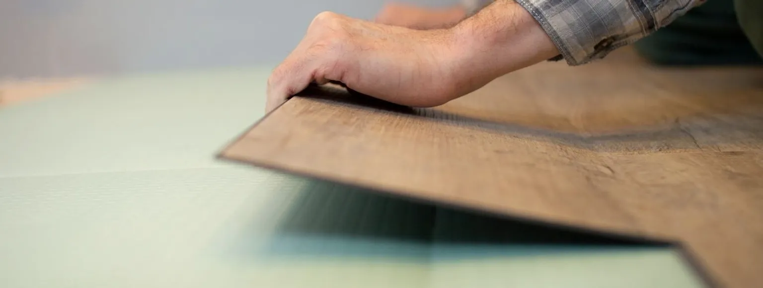 Die Hände einer Person verlegen schwimmend verlegte Vinyl-Bodenbeläge auf einer grünen Unterlage.