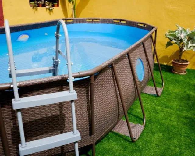 Ein brauner Gartenpool mit einer Metallleiter steht auf grünem Kunstrasen im Freien.