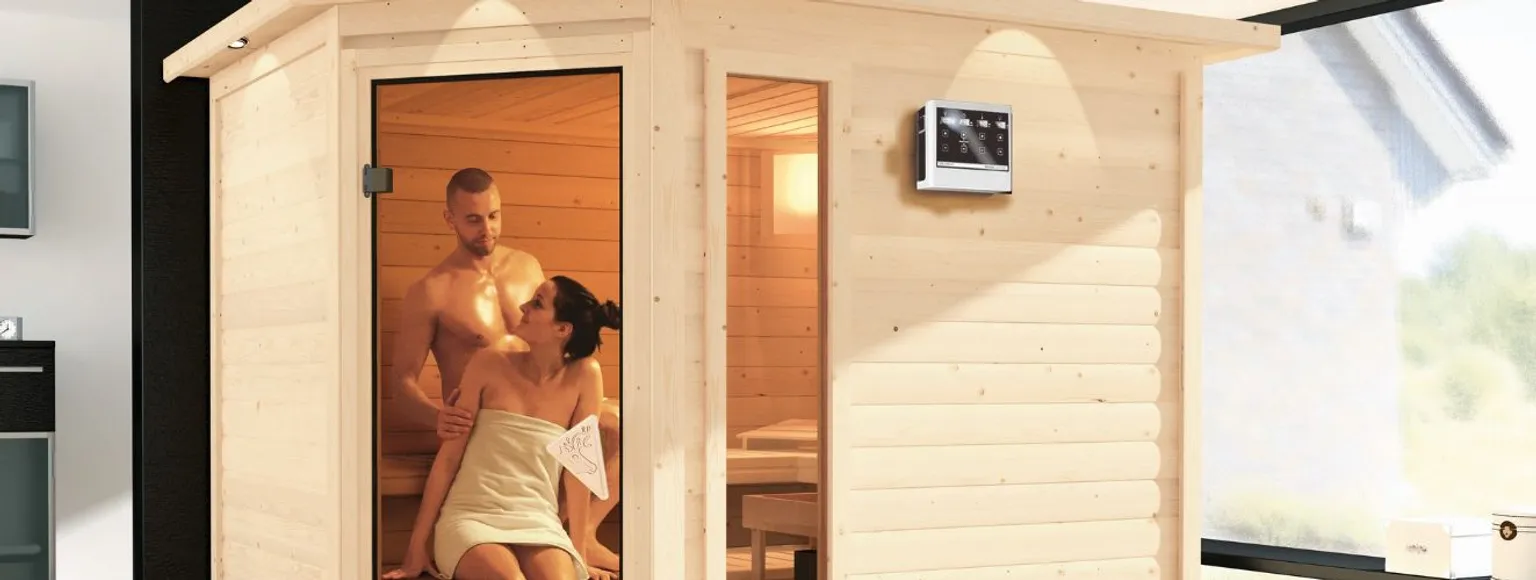 Ein Mann und eine Frau sitzen zusammen in einer hellen Holzsauna mit Sitzbänken und holzgetäfelten Wänden.