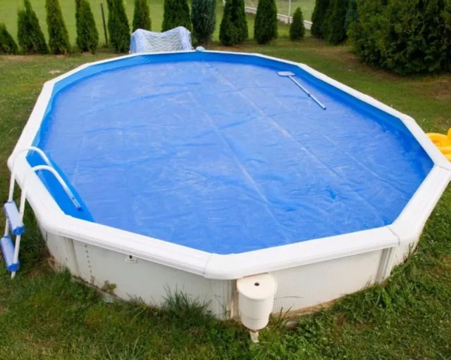 Ein rechteckiger Gartenpool mit blauer Abdeckung auf grünem Gras in einem Hinterhof.
