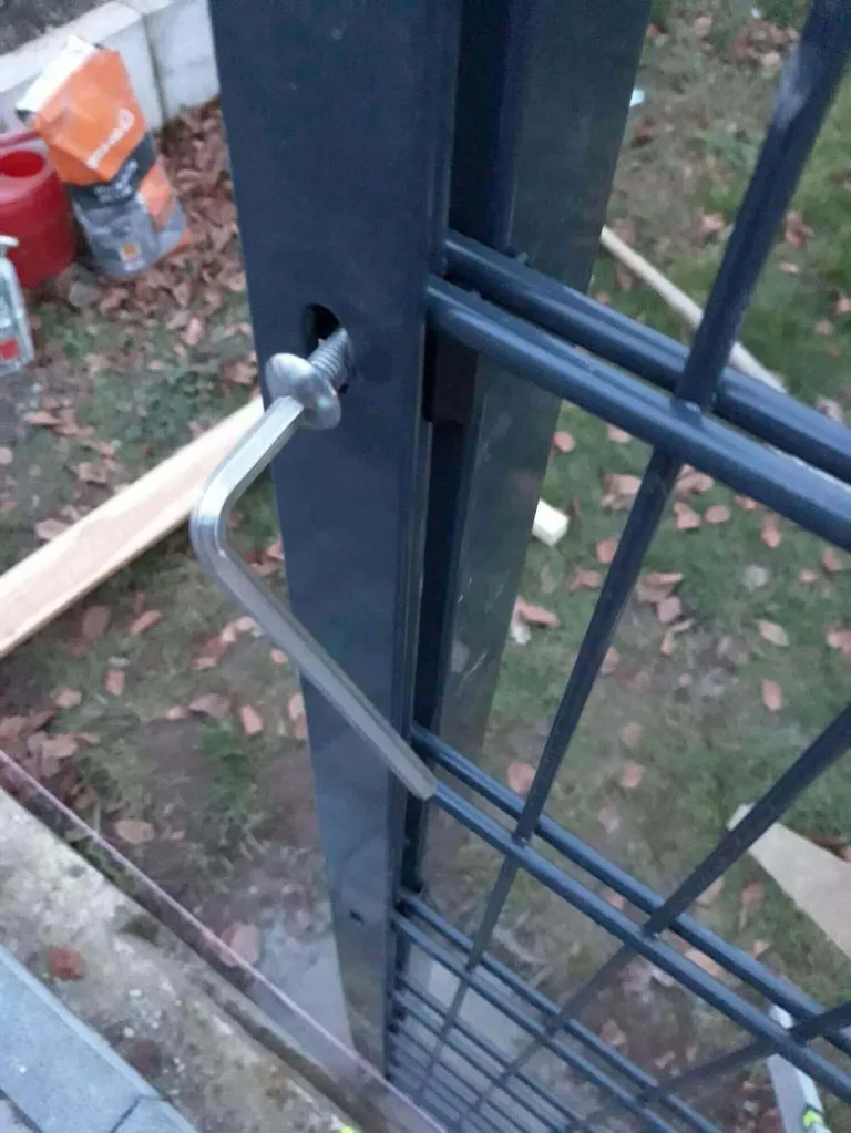 Ein silberner Sechskantschlüssel steckte in einem grauen Metallpfosten neben grünem Gras und Werkzeugen.