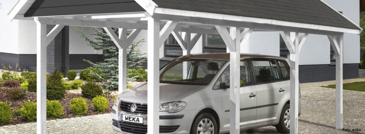 Ein silberner Volkswagen parkte unter einem weißen Holzcarport neben einem Wohnhaus.