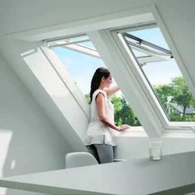 Eine Frau in einem modernen Zimmer öffnet ein großes Oberlichtfenster, durch das natürliches Licht einfällt.