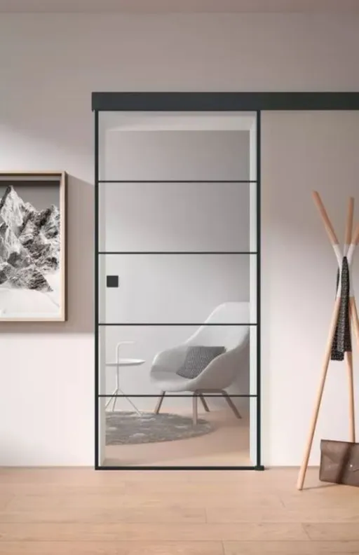 Eine Glasschiebetür führt in einen Raum mit einem grauen Stuhl und gerahmten Kunstwerken an der Wand.