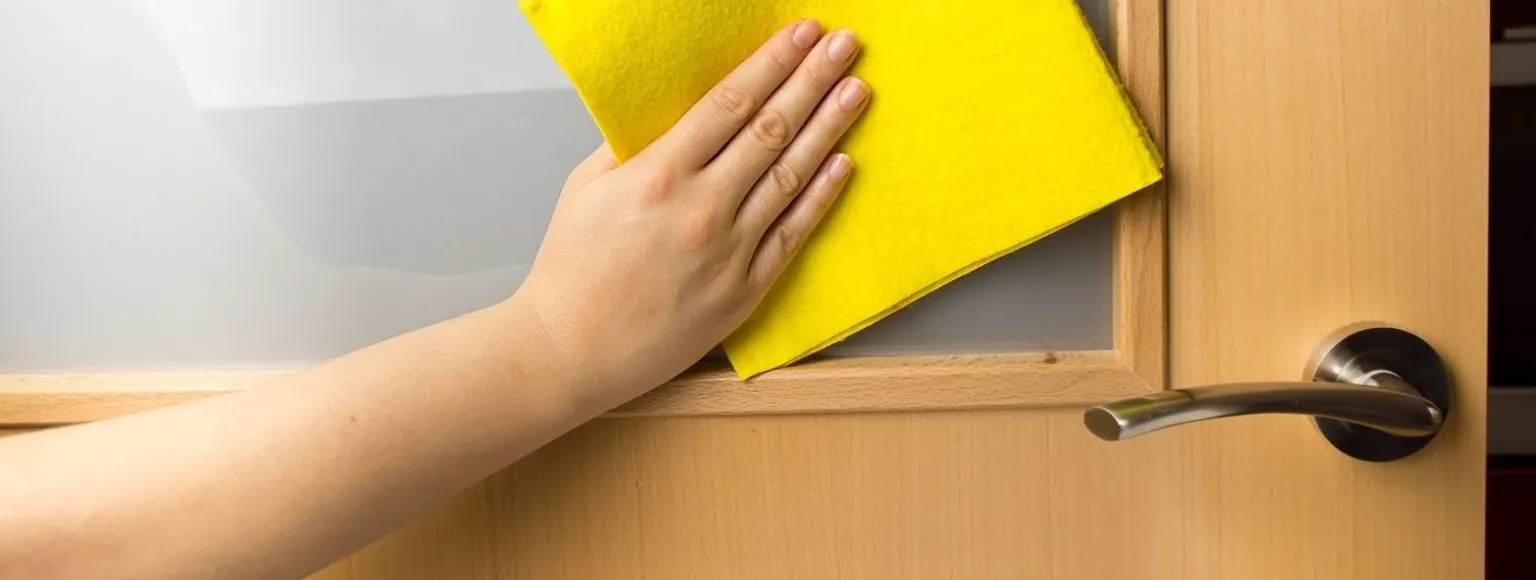 Eine Hand reinigt eine Holzzimmertür mit gelbem Tuch am silbernen Türgriff.