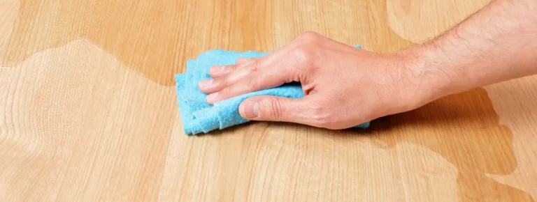 Eine Hand wischt verschüttete Flüssigkeit von einem hellen Holzboden.