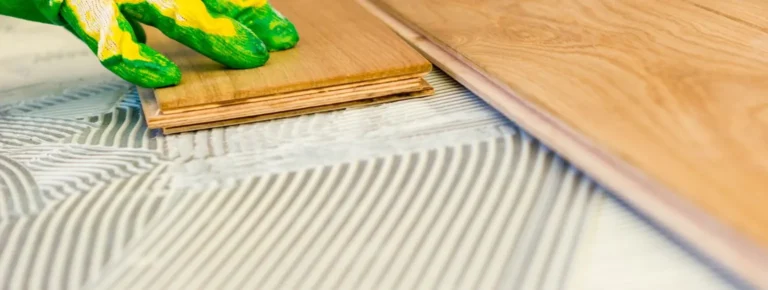 Person drückt Holzparkettboden mit Handschuh auf Klebstoff
