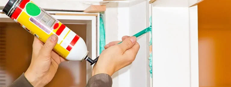 Eine Person, die einen weißen Fensterrahmen mit Dichtungsmasse abdichtet.