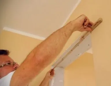 Eine Person misst mit einem Lineal eine weiße Wand, um Maße für den Türausschnitt anzupassen.