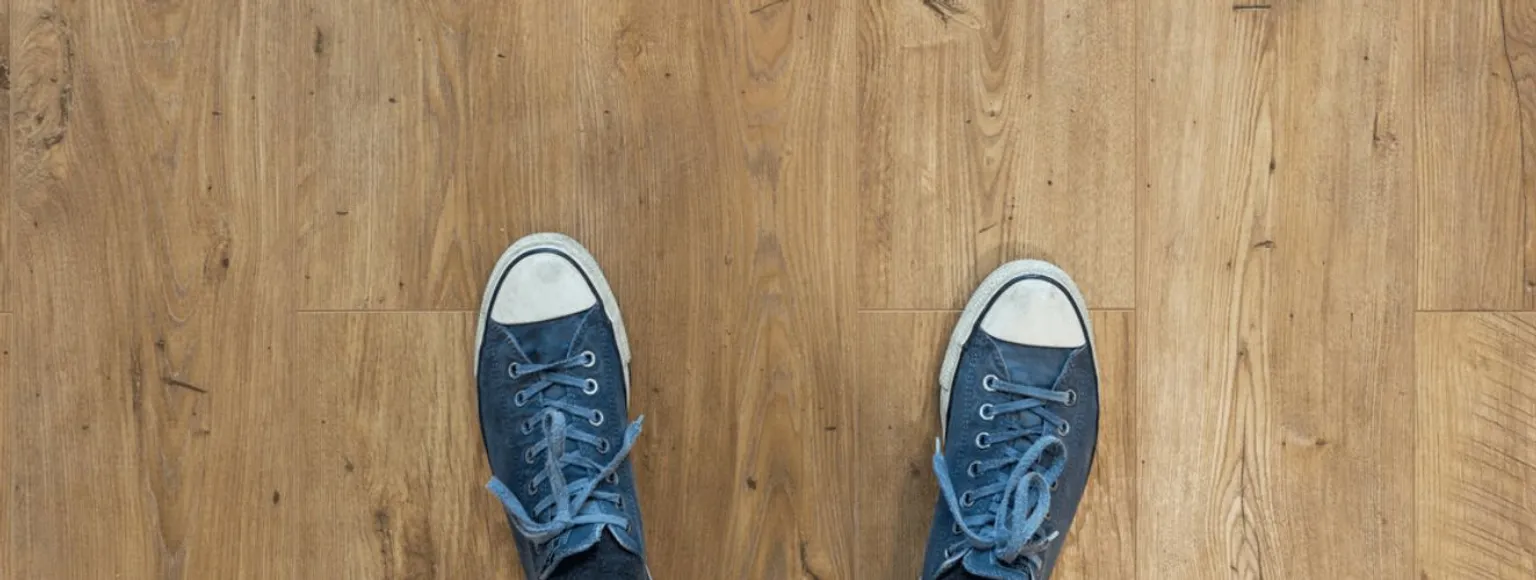 Eine Person mit blauen Sneakers steht auf hellbraunem Parkettboden, aus der Vogelperspektive.