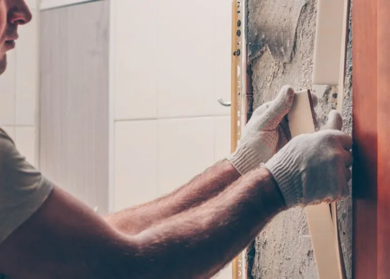 Eine Person mit Handschuhen entfernt eine weiße Wandverkleidung von einer Innenwand.