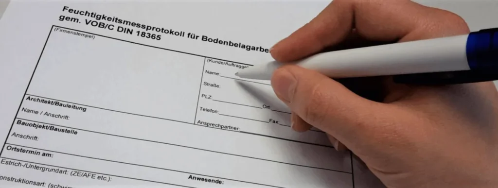 Eine Person schreibt mit einem blauen Stift auf einem Tisch in ein Formular zur.