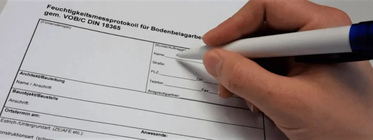 Eine Person schreibt mit einem blauen Stift auf einem Tisch in ein Formular zur.