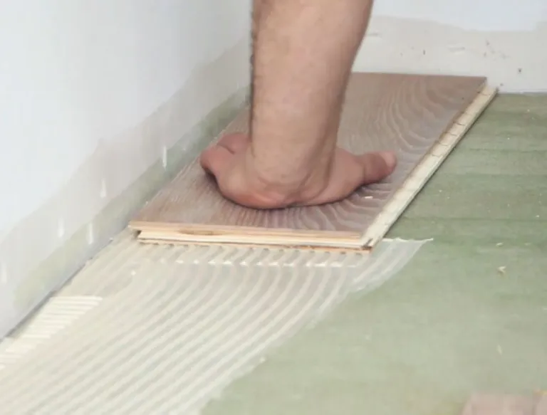 Eine Person verlegt hellbraune Dielen an einer weißen Wand und folgt dabei den Schritten des Parkettführers.