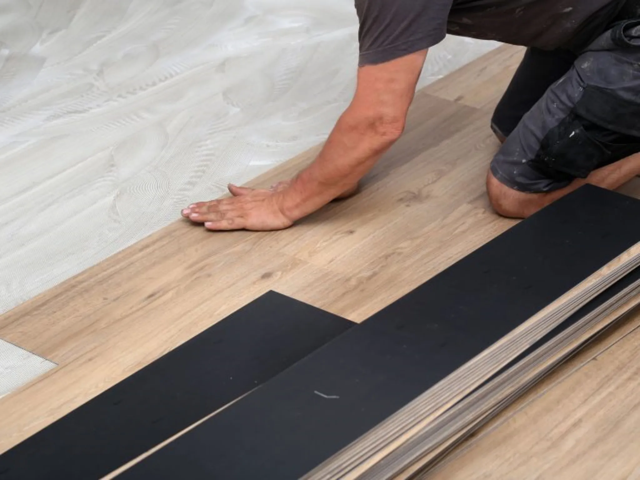 Eine Person verlegt Vinylboden kleben auf Kleber, mit leichten Holzlaminatdielen an ihrer Seite.