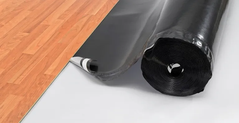 Eine schwarze Dampfsperrrolle liegt neben einem teilweise verlegten hellbraunen Parkettboden.