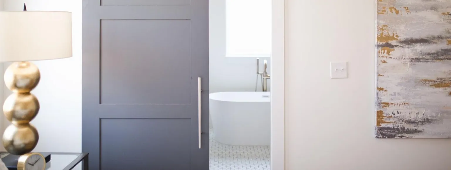 Eine teilweise geöffnete graue Schiebetür gibt den Blick frei auf ein weißes Badezimmer mit einer Badewanne im Inneren.