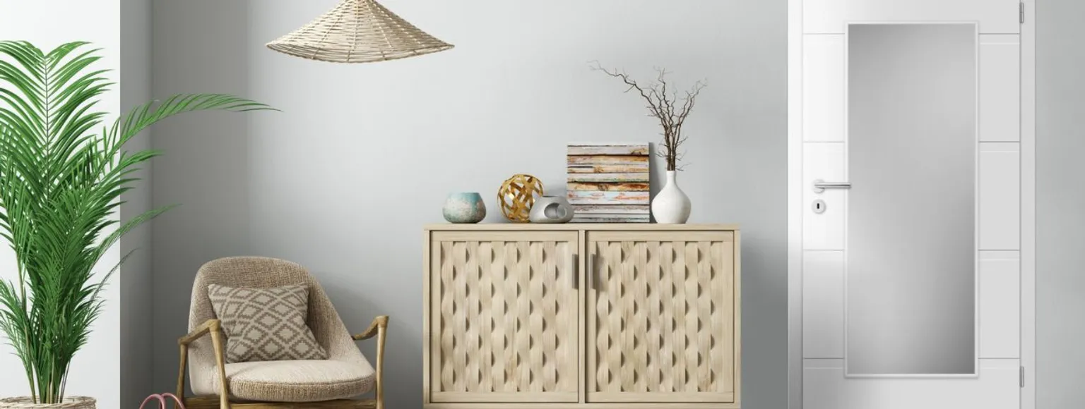 Eingangsbereich in neutralen Farben mit Korbsessel, hellem Holzschrank, Pflanzen und Dekorplatten.