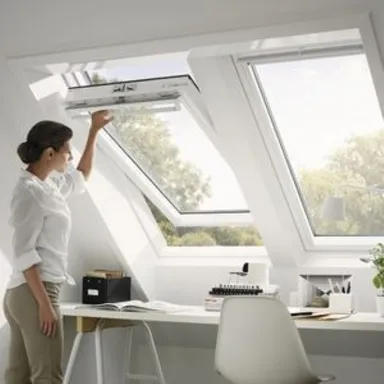 Frau im Dachgeschoss Büro öffnet ein Oberlicht Fenster mit weißen Wänden und hölzernen Schreibtisch sichtbar.
