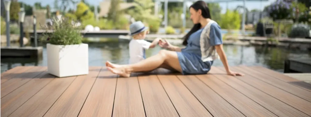 Frau und Kind sitzen auf einem grauen WPC-Deck am Wasser, umgeben von der Natur.