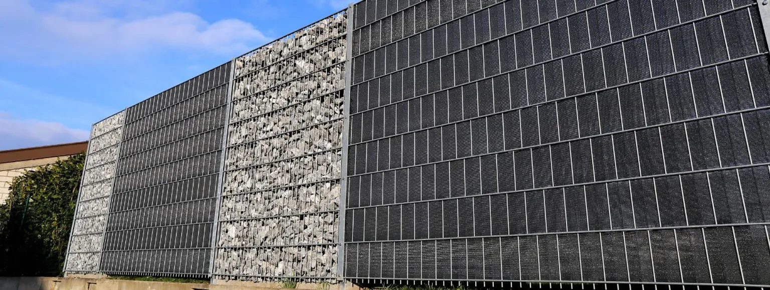 Gabionenzaun aus Metallgitterplatten und grauen Steinkörben, Außenanlage.