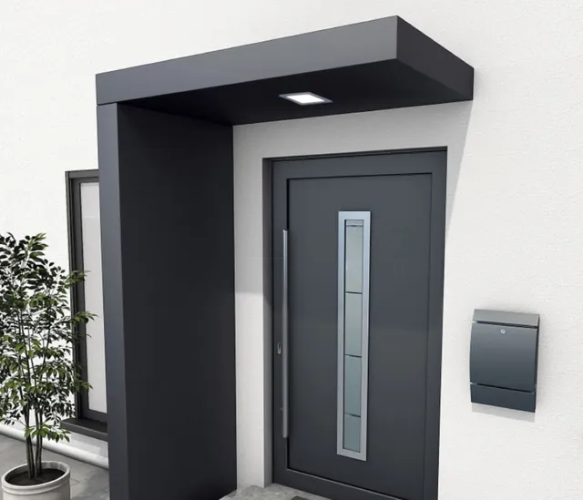 Graue, moderne Haustür mit passendem Vordach, Briefkasten und einer Topfpflanze neben dem Eingang.