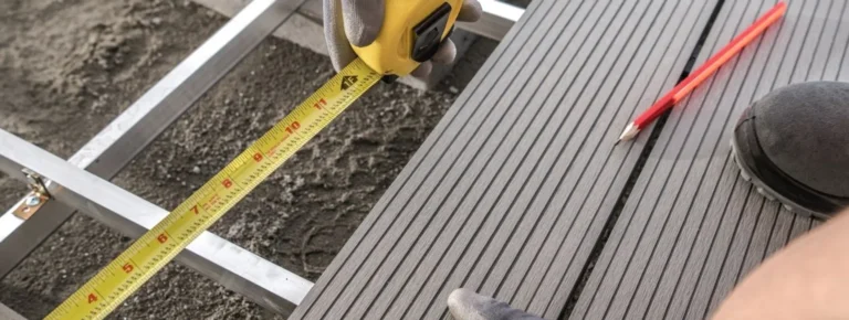 Handschuhe benutzen ein Maßband auf grauen WPC-Terrassendielen.