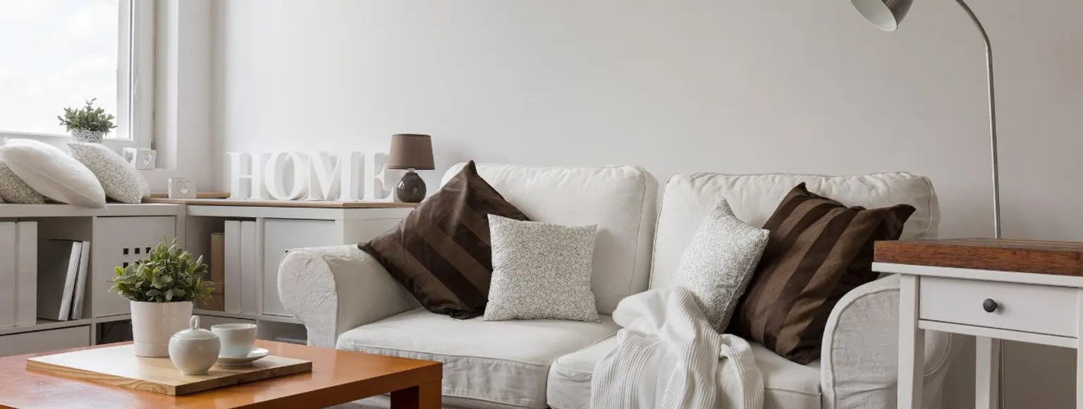 Helles Wohnzimmer mit weißem Sofa, hellen Wänden und Bodenbelägen, geeignet für kleine Räume.