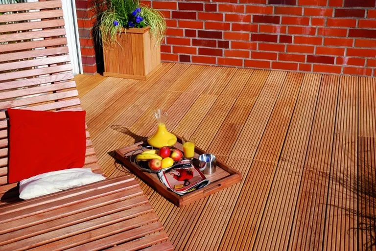 Holzterrasse mit Hartholzbelag, Liegestuhl, Obstschale und Grünpflanzen im Hintergrund.