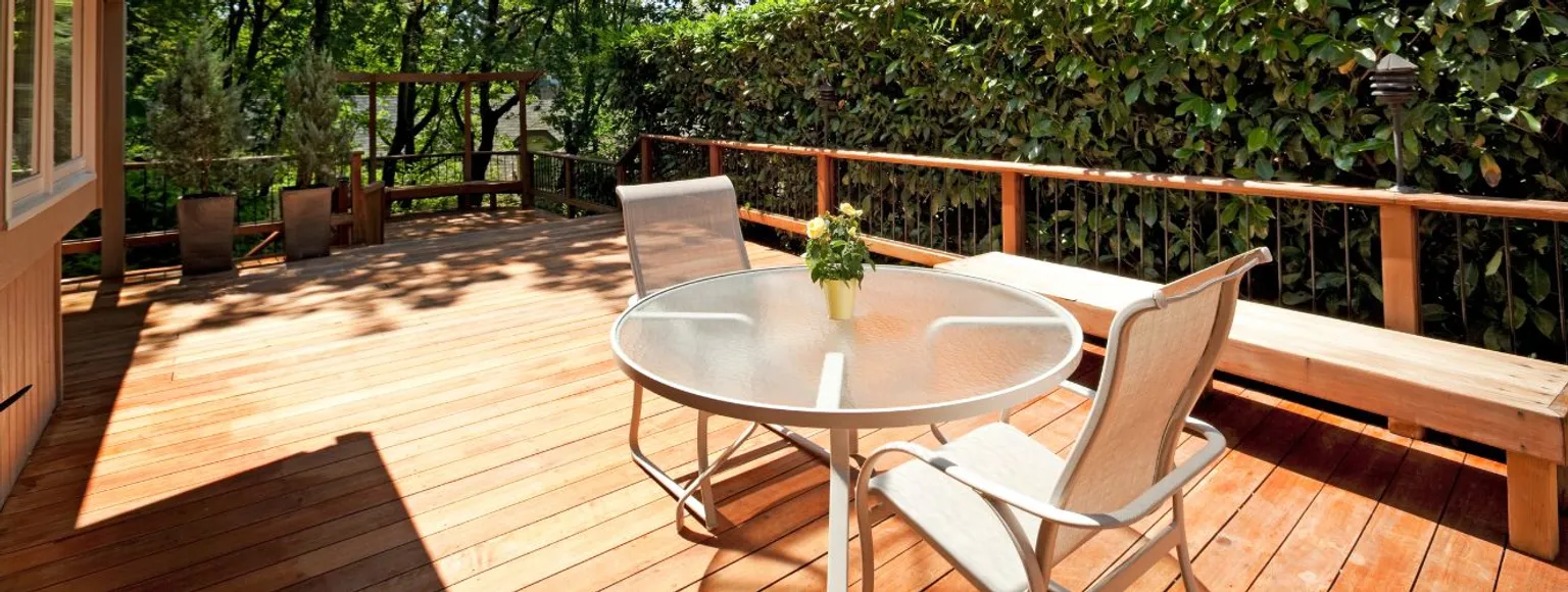 Holzterrasse mit Terrassendielen aus Hartholz, Tisch und Stühle im Freien, Pflanzen im Sonnenlicht.