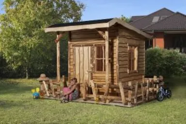 Kinderspielhaus aus Holz mit Spielgeräten auf grünem Rasen in einer Gartenanlage.