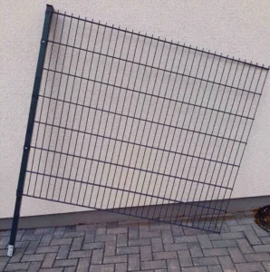 Metallzaun mit Doppelstabmatten steht schräg an einer hellen Mauer.