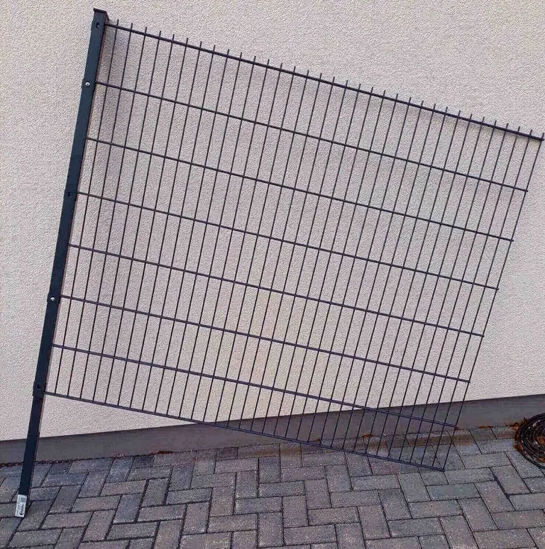 Metallzaun mit Doppelstabmatten steht schräg an einer hellen Mauer im Innenbereich.