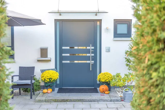 Moderne blaue Eingangstür mit gelben Blumen und Kürbissen vor der Tür, Blick ins Freie.