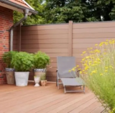 Moderne Terrasse mit einem grauen Loungesessel, mehreren grünen Topfpflanzen und einem Sichtschutzzaun aus Holz.