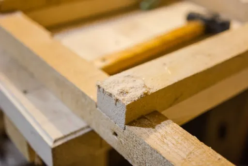 Nahaufnahme von hellbraunen Holzbrettern und einem silbernen Hammer auf einer Werkstattfläche.
