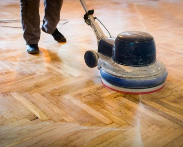Person, die eine Bodenpuffermaschine zum Schleifen und Polieren heller Holzdielen in einem Raum verwendet.