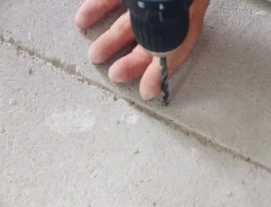 Person, die einen schwarz-blauen Bohrer in der Nähe eines grauen Betonbodens benutzt, um ein Übergangsprofil zu installieren.